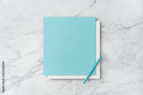 Top view of blank white and blue square greeting card with pencil mockup on marble background with copy space