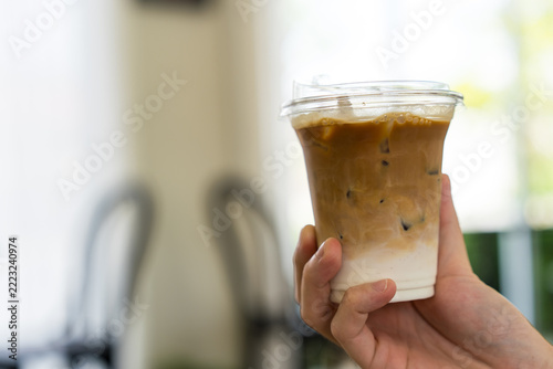 Hand holding a glass of iced latte coffee with two layers of fresh milk and espresso shot. Refreshing summer drink concept