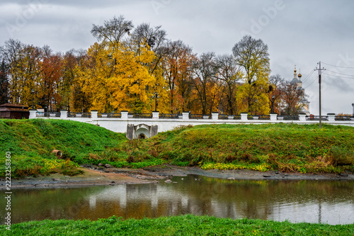 A white stone ancient bridge over a river, set against a backdrop of trees with yellow autumn foliage.