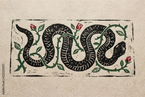 Detailed handcrafted traditional linocut relief block print artwork on textured beige paper featuring a coiled black snake intertwined with thorny green vines and romantic red roses.