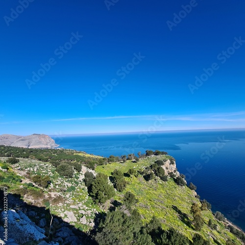  Spectacular panoramic view of a coastal hillside covered with Mediterranean vegetation overlooking crystal-clear blue waters. Scenic natural landscape in southern Italy.
