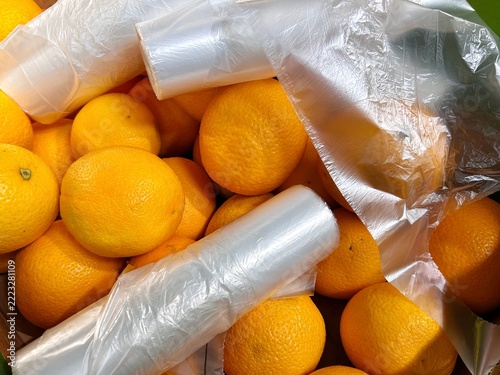 Rolls of disposable plastic produce bags lie on top of loose oranges in a supermarket display, highlighting unnecessary packaging and excessive plastic consumption 