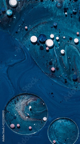 Macro abstract photography featuring deep blue and turquoise liquid paint swirling with organic fluid textures and shimmering metallic glitter dust particles creating a celestial cosmos atmo