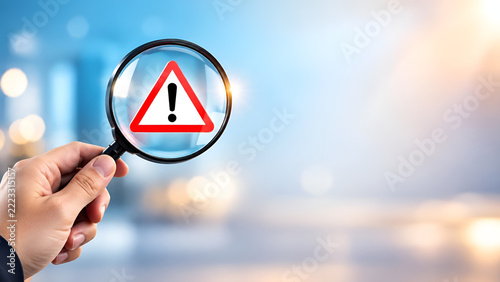Magnifying glass highlighting attention sign in blurred background, symbolizing risk assessment and caution in business and safety environments.