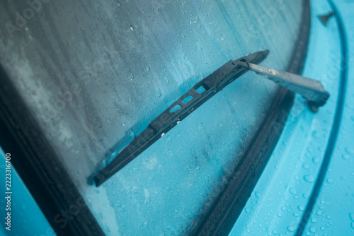 Close up of vintage blue car windshield wiper on misty glass with raindrops.
A high-quality close-up photograph focusing on the classic metal windshield wiper arm and rubber blade 