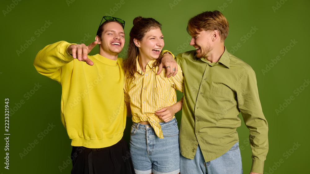 Fototapeta premium Smiling young companions embracing shoulders against green studio backdrop with warm affection. Social belonging, friendship support, emotional connection concept.