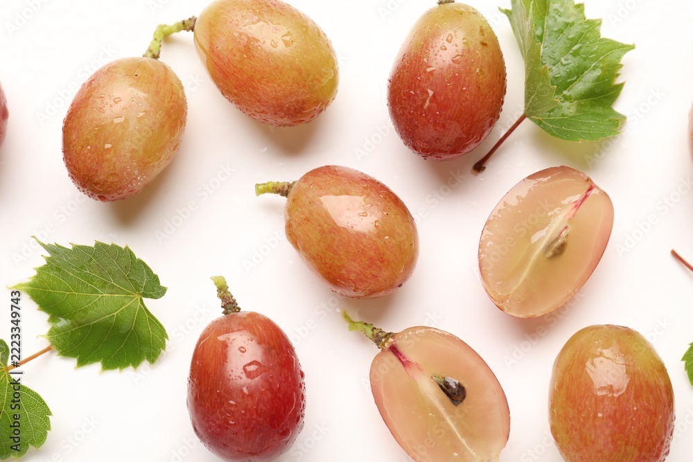 Fototapeta premium Fresh ripe grapes and green leaves on white background, flat lay