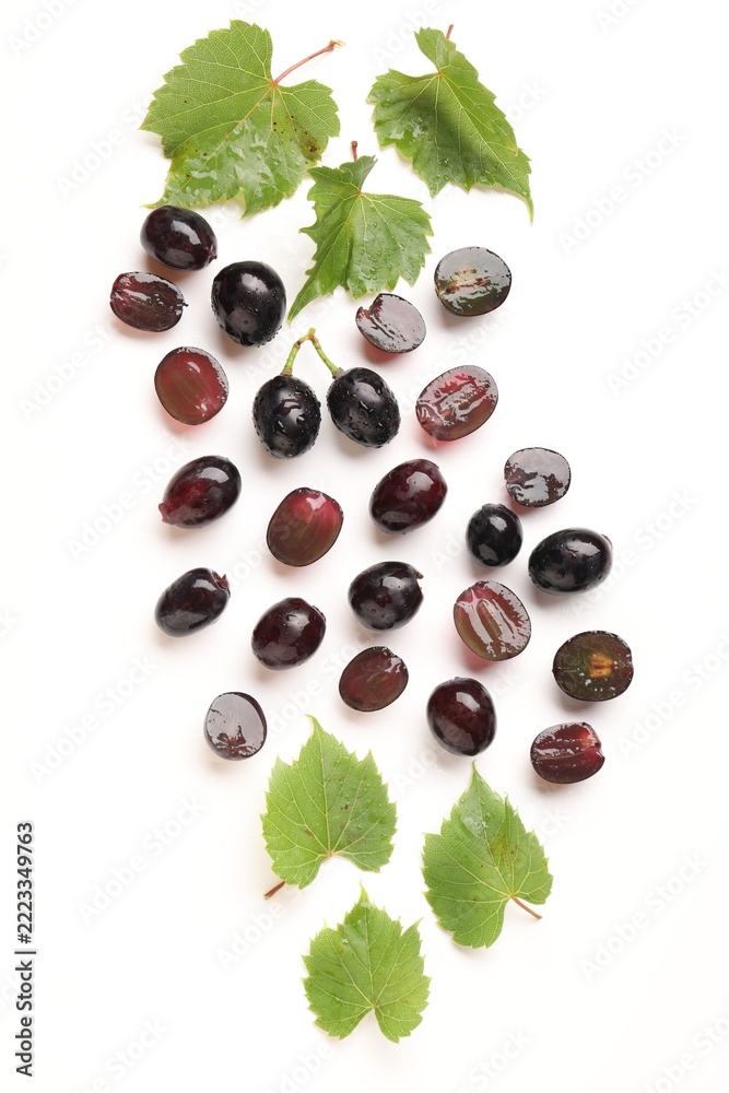 Fototapeta premium Fresh ripe grapes and green leaves on white background, flat lay