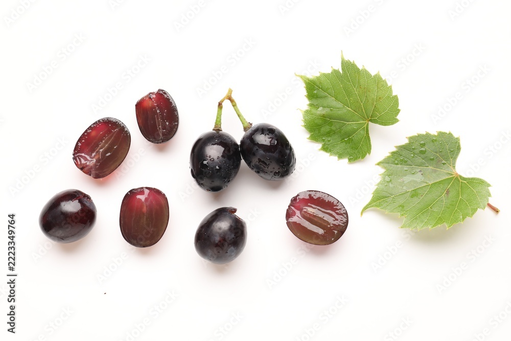 Fototapeta premium Fresh ripe grapes and green leaves on white background, flat lay