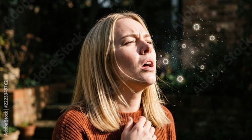Adult woman sneezing beside graphic bacteria in green park with distressed expression. Seasonal health editorial, pharmacy services, respiratory education concept.