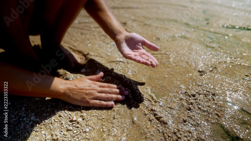 Woman touching wet sand beside shallow seawater