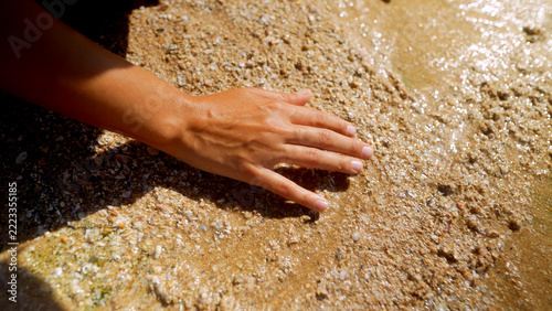 Close-up of a woman's hand touching wet beach sand