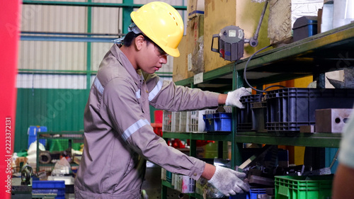 Industrial worker inspecting and handling parts on storage shelves in a manufacturing factory.