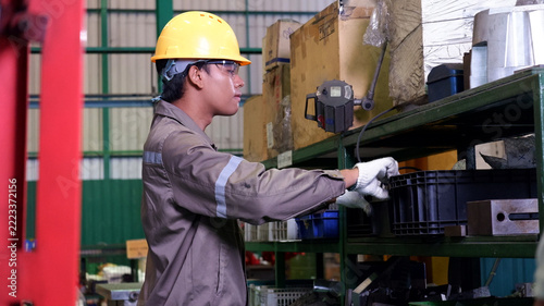 Industrial worker inspecting and handling parts on storage shelves in a manufacturing factory.