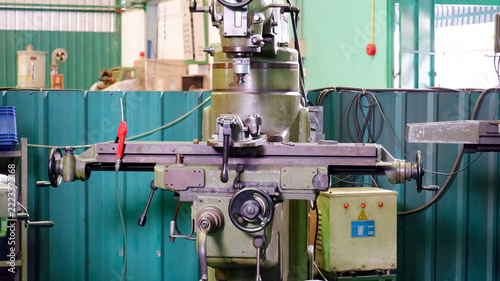 Industrial metal milling machine with a control panel and mechanical components inside a manufacturing factory.