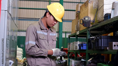 Industrial worker inspecting and handling parts on storage shelves in a manufacturing factory.