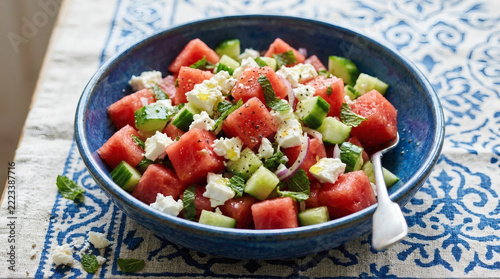 Refreshing summer watermelon and feta salad with cucumber and mint served in a rustic blue ceramic bowl.