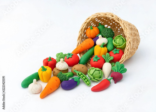 A small tippedover wicker basket spilling colorful toy vegetables onto a white surface