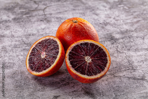 Fotografie Fresh blood oranges, whole fruit and two halves with deep red flesh on grey ston