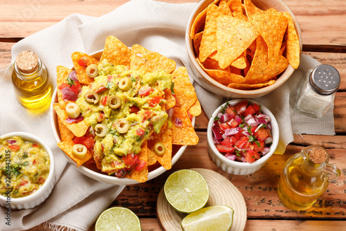 Mexican nachos tortilla chips in a ceramic bowl, topped with guacamole, chopped tomatoes, and green olives.