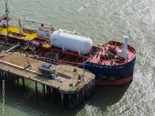 Aerial view of a tanker ship docked at a concrete pier with a large white cylindrical tank on its deck in the United Kingdom.
