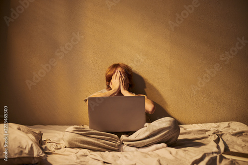 Caucasian young adult sitting with laptop covering face showing digital fatigue. Visual ideal for mental health awareness campaigns and remote working stress articles