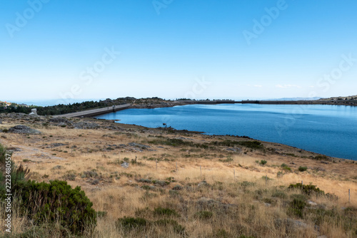 Vista panorâmica da albufeira da Barragem da Lagoa Comprida num dia de verão com vegetação rasteira e um céu límpido em Portugal