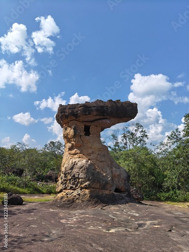 Mushroom Rock Formation: A unique, naturally formed mushroom-shaped rock stands majestically under a bright blue sky with scattered clouds, surrounded by sparse vegetation and rocky terrain.