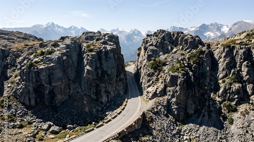 Aerial view of a scenic winding road cutting through a narrow rock pass in the Rocky Mountains with snow-capped peaks in the distance