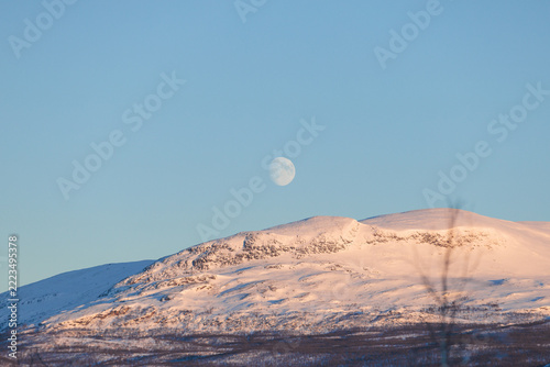 Obraz na plátně Full moon above snow covered mountains in Kiruna, Swedish Lapland, Sweden