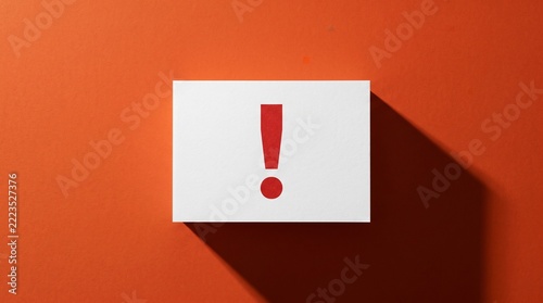 Exclamation mark on white paper card against orange background. Minimalist conceptual photograph showing a bold red warning sign on a clean rectangular surface with sharp shadows for business alert