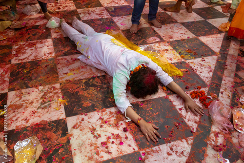 Person lying prostrate in prayer on a checkered floor strewn with petals during Lathmar Holi, Barsana, India