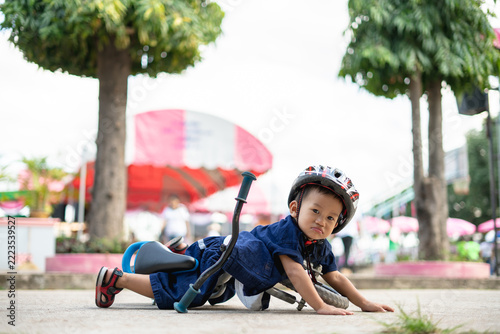 Asian 2 years old boy wearing a helmet, lying on the ground after falling from his balance bike.