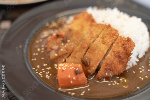 Japanese curry rice with crispy pork cutlet, served with flavorful curry sauce, carrots, and sesame garnish.