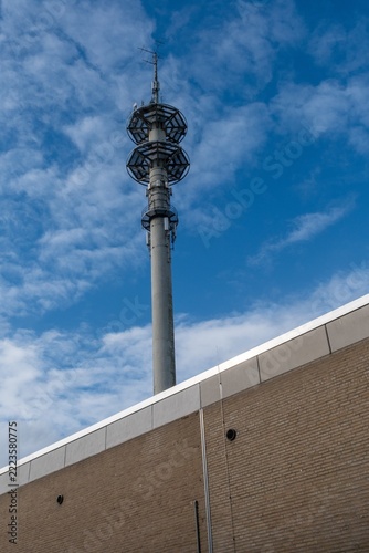 Tall communication tower near building under blue sky with clouds