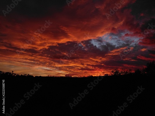 Dramatic fiery sunset sky backdrop with moody crimson clouds and minimal dark silhouette foreground copy space for text
