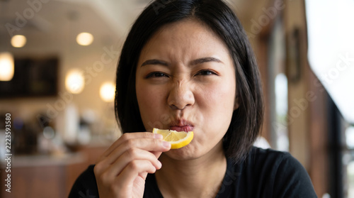 Close up of woman eating sour lemon slice with puckered face and squinted eyes, sour taste reaction in cafe restaurant
