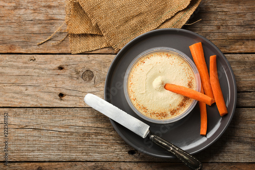 Enjoying Hummus With Carrot Sticks on a Wooden Table