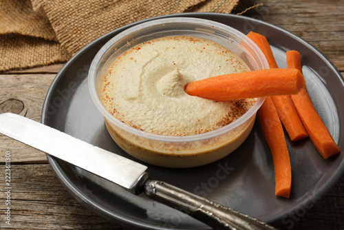 Enjoying Hummus With Carrot Sticks on a Wooden Table
