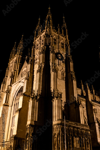 Night time view of the spires and towers at the entrance of the majestic gothic Canterbury Cathedral, illuminated against the black night sky.