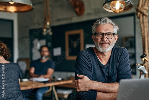 Mature entrepreneur wearing glasses posing confidently with arms crossed in a creative workspace
