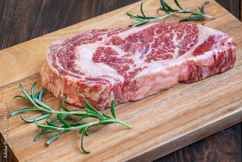 Raw Wagyu ribeye steak with intricate marbling and fresh rosemary on wooden board