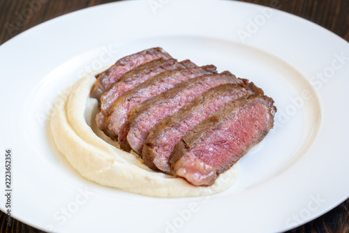 Sliced medium rare Wagyu steak over creamy celery root puree on porcelain plate