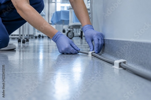 Gloved hands securing a cable along an operating room wall