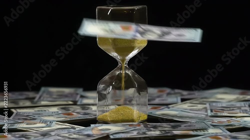 Beneficial Banking Terms. Hourglass with golden sand stand among the falling banknotes. Around are already scattered a lot of dollar bills