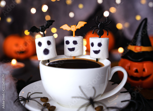 A spooky Halloween coffee setup featuring playful marshmallow ghost toppers, tiny spiders, and seasonal pumpkin decorations, perfect for a fun autumn celebration. Close-up.