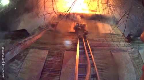 several firefighters start extinguishing a wooden two-story apartment building with fire hoses in the summer
