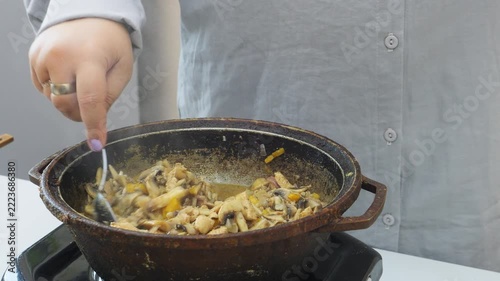 In a deep cast-iron skillet, onions and chicken are simmered in a sauce and spices with mushrooms and tomatoes. Medium shot.