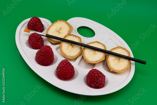 Fotografie Creative Fruit Art Palette with Raspberries, Banana Slices and Paintbrush on Gre
