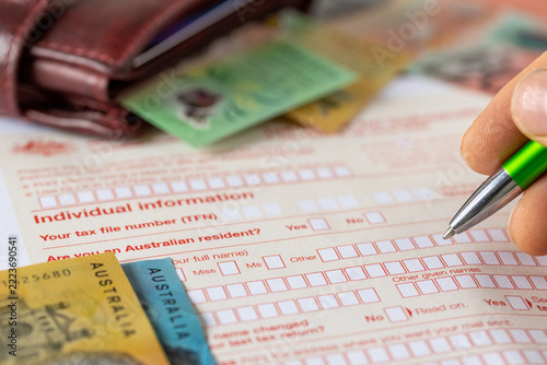 Filing a tax return in Australia – deadline. Financial concept. Tax form, wallet, and a hand holding a pen. Business background, close-up.